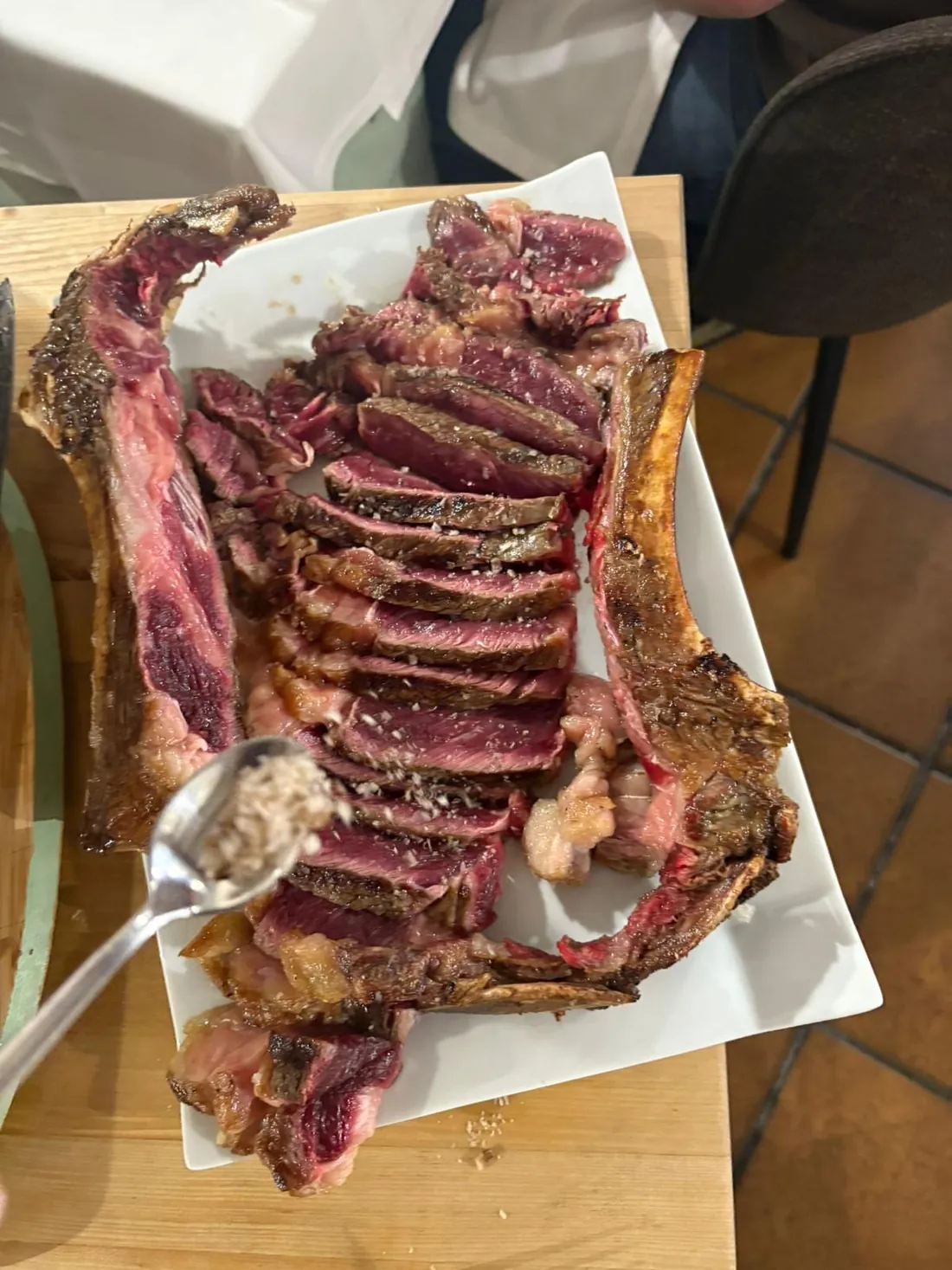 Un chuletón madurado cortado en tiras junto a su hueso, sobre una fuente blanca