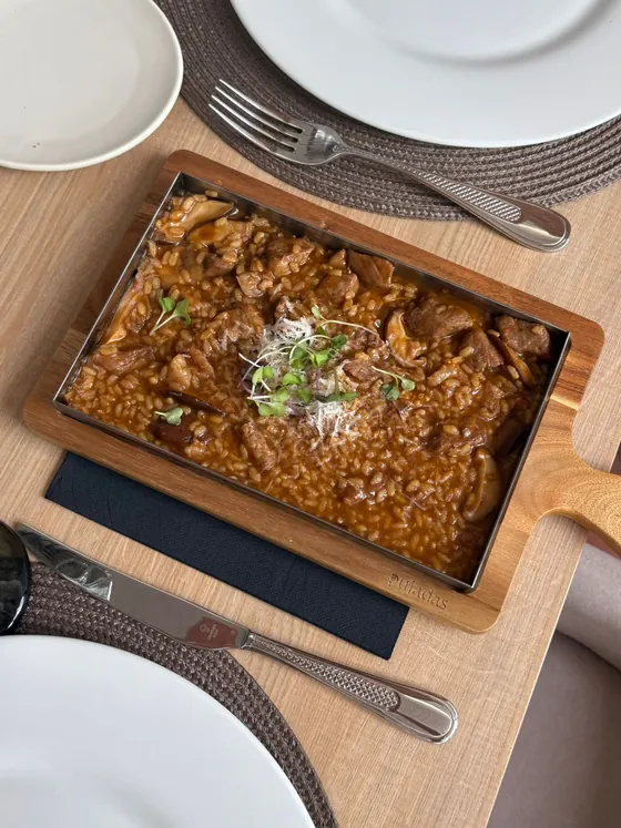 Un guiso de carne servido en una fuente de madera sobre la mesa puesta