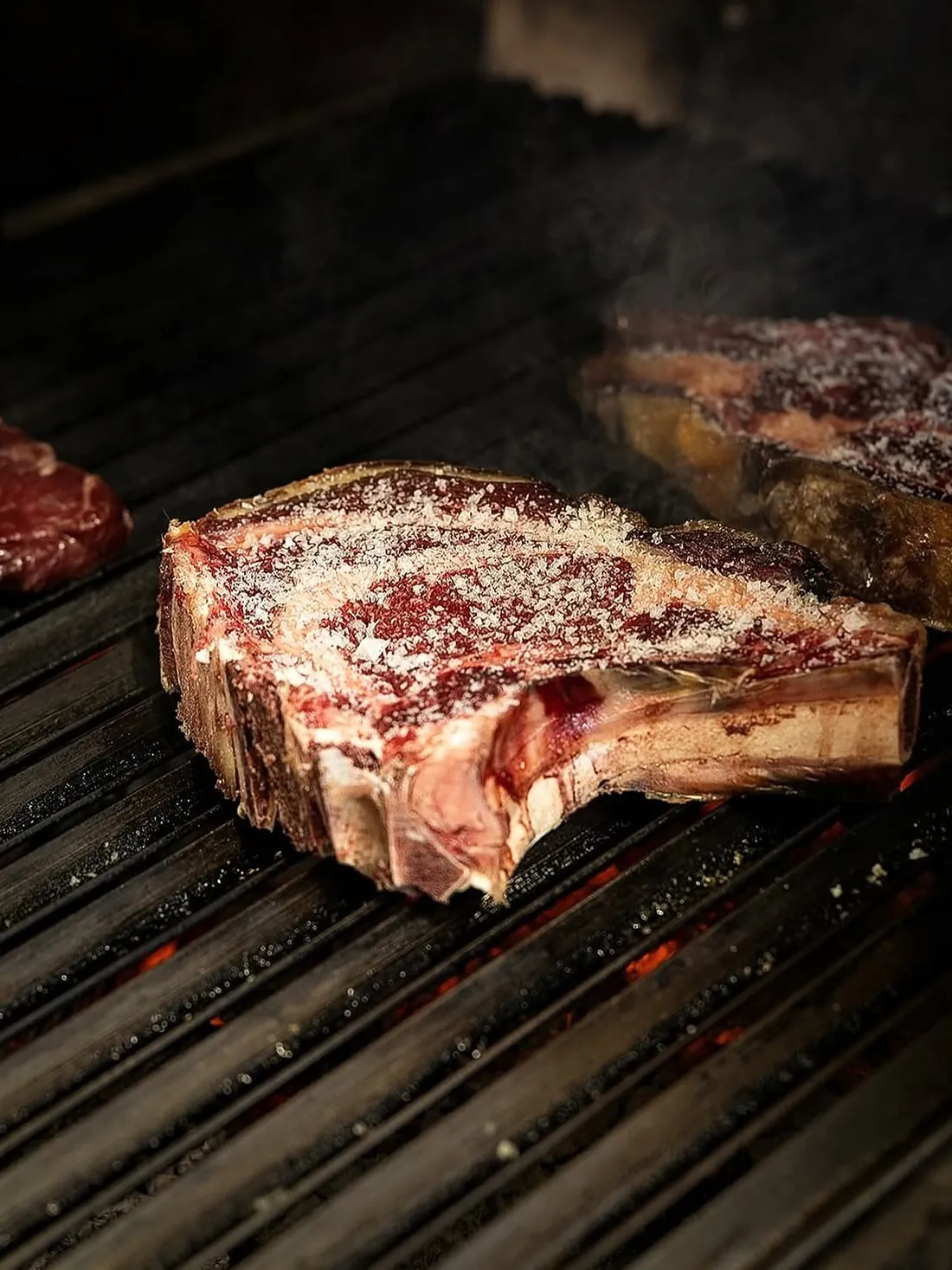 Un chuletón madurado sobre la parrilla, con otra pieza al fondo