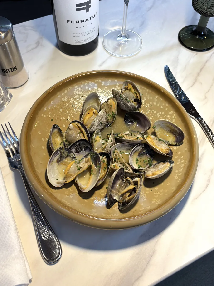 Almejas a la sartén en un plato hondo, junto a una botella de vino