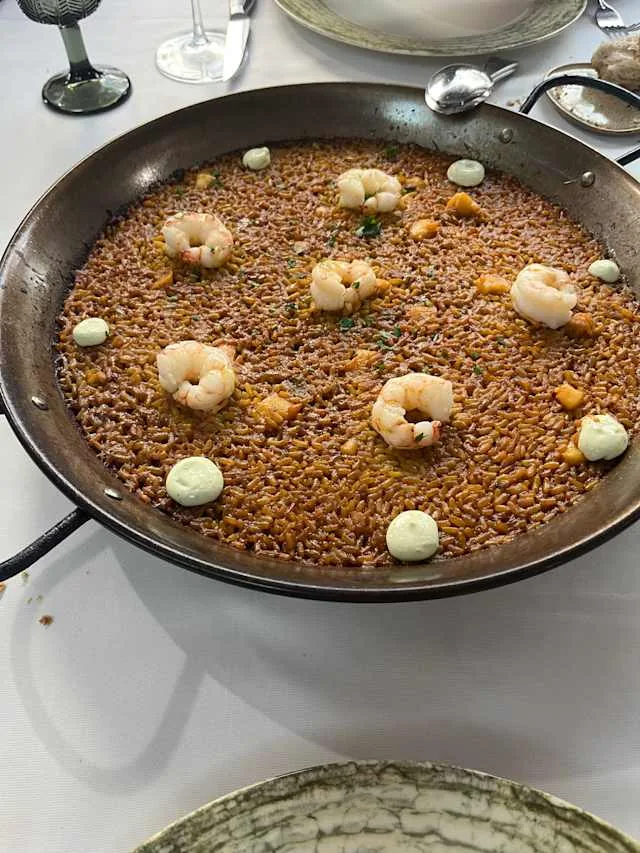 Un arroz en su paella con gambas peladas y puntos de alioli, sobre un mantel blanco